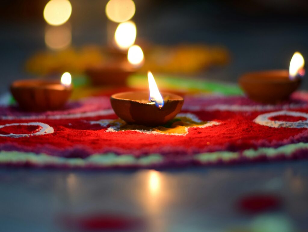 Lit diyas placed on colorful rangoli, creating a warm ambiance for Diwali celebrations.